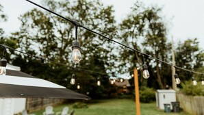 Ein Garten mit Lichterketten, Sonnenschirm und Gartenmöbeln.