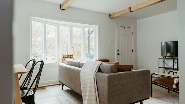 Ein Wohnzimmer mit Sofa, Fernseher und einem Fenster mit Blick auf Bäume.
