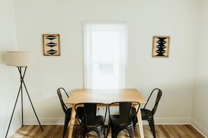 Ein Essbereich mit einem Holztisch, vier schwarzen Stühlen, einer Stehlampe und zwei abstrakten Bildern an der Wand.