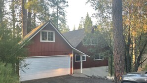 Une maison à deux étages, avec une façade rouge et des portes de garage blanches, entourée d’arbres et bordée d’une allée en gravier.