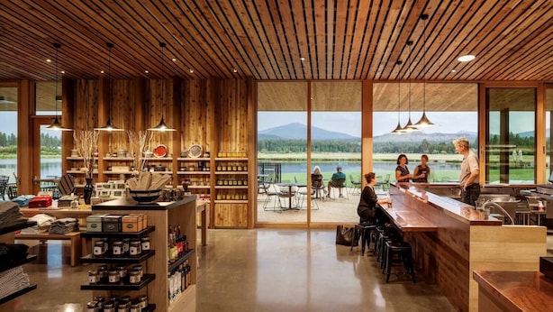 A modern interior with wooden paneling, a bar area, and large windows overlooking a lake. - Modern Black Butte Abode (Sisters)