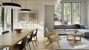 A modern interior with a dining area, sofa, and large windows offering a view of the outdoors. - Modern Black Butte Abode (Sisters)