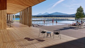 An outdoor wooden deck with a pool, lounge chairs, and a view of mountains and a lake. - Modern Black Butte Abode (Sisters)
