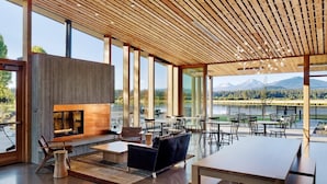 A spacious living area with a fireplace, modern furniture, and large windows offering a scenic view of a lake and mountains. - Modern Black Butte Abode (Sisters)