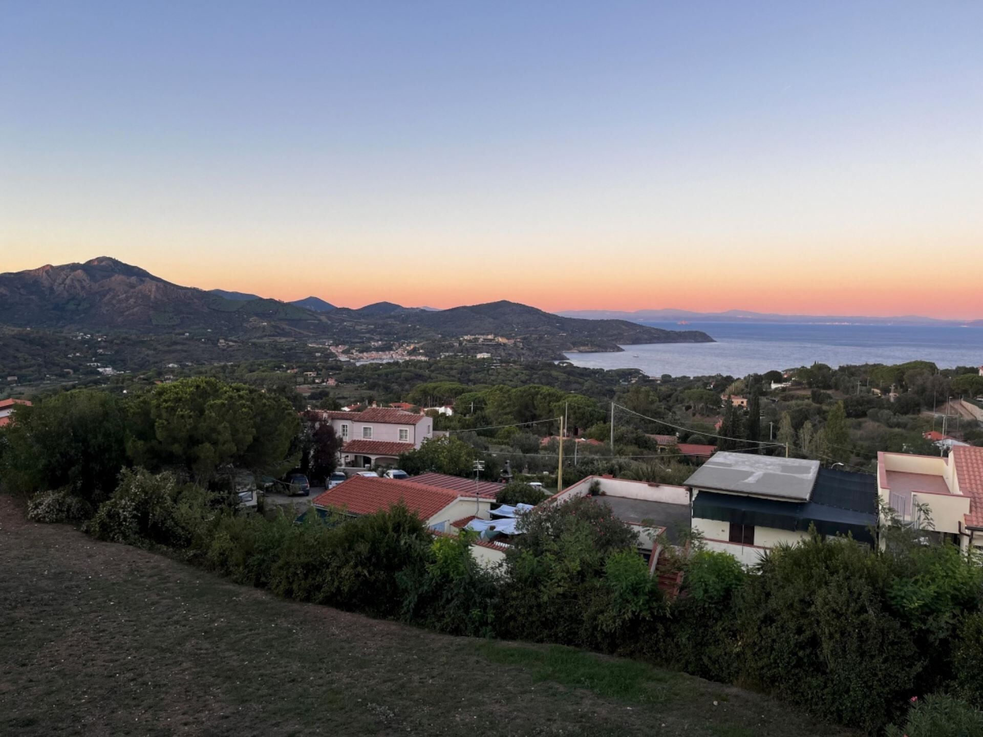 A coastal town with houses, a mountain range, and a view of the sea.