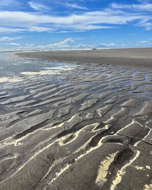 A beach with patterned sand formations and a clear sky.