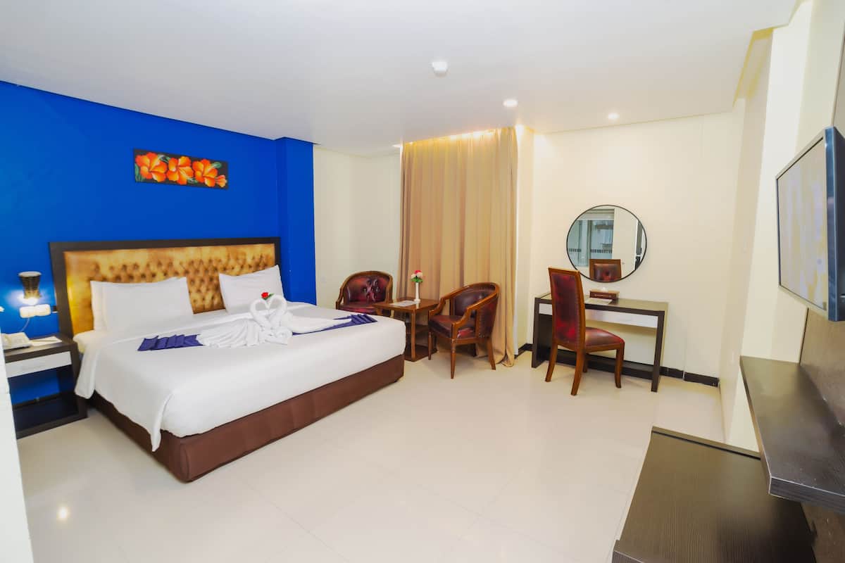 Een hotelkamer met een groot bed, een bureau, een stoel, een televisie en een spiegel.