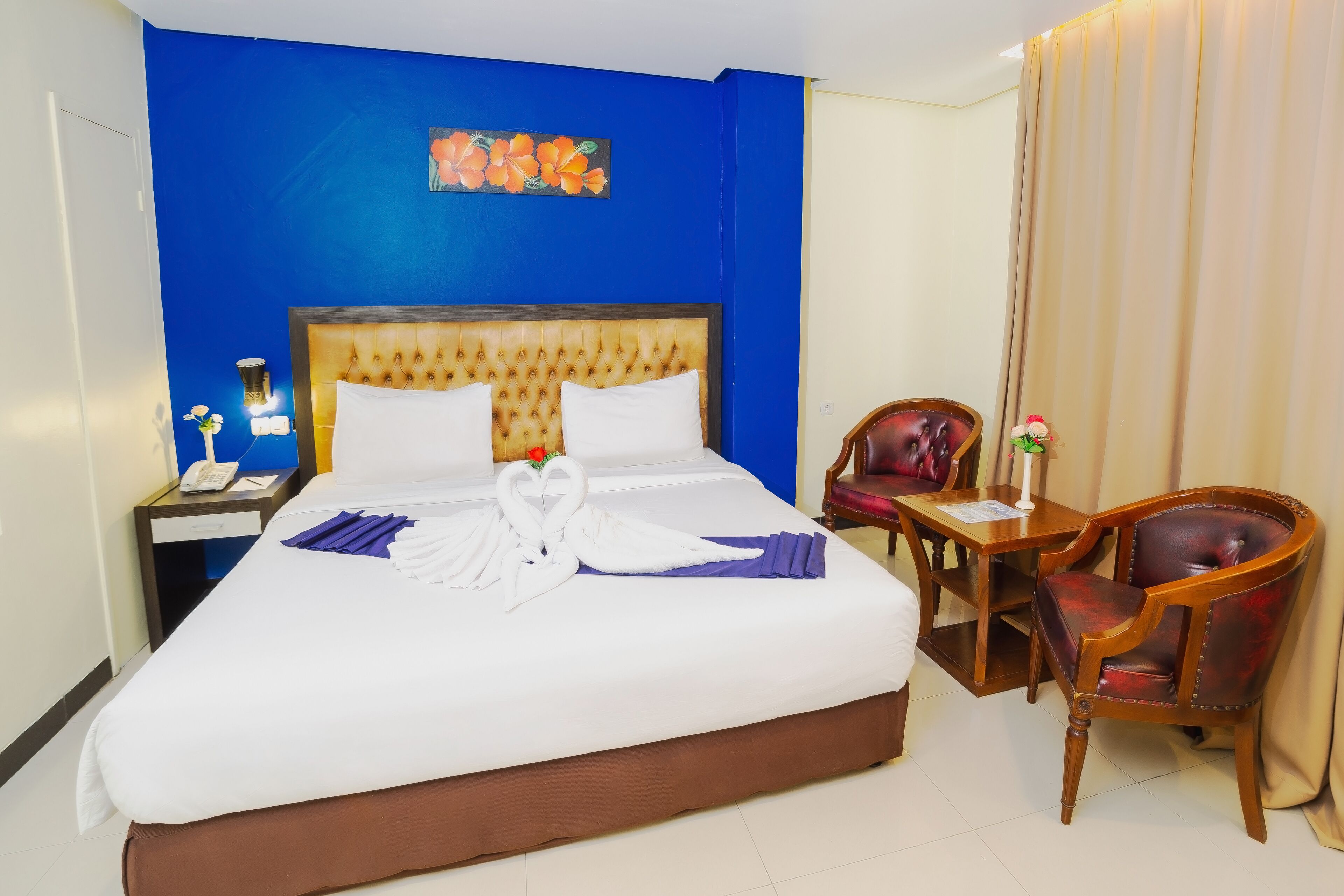 Ein Hotelzimmer mit einem großen Bett, einem hölzernen Kopfteil, einem Schreibtisch mit Stuhl und einer blauen Wand mit einem Blumenbild.