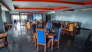 Een modern restaurant met een marmeren wand, houten tafels, blauwe stoelen en een licht plafond.