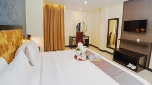 Hotelkamer met een groot bed, nachtkastje met een bloevas, spiegel, televisie en schoenenrek.