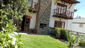 A two-story house with a stone facade, wooden balconies, and a small garden area.