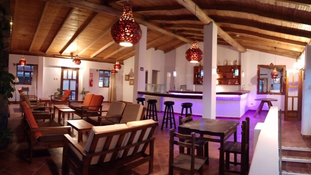 A spacious living area with wooden furniture, a kitchen area with a bar, and hanging pendant lights.