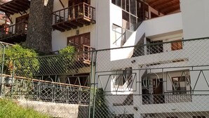 A multi-story building with balconies, a stone chimney, and a metal fence.