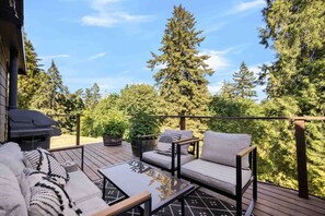 Una terraza con mobiliario exterior, una parrilla y vistas a árboles altos.
