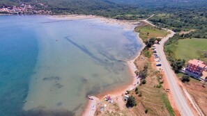 An aerial view of a coastal area with a beach, parked cars, and buildings along the shore. - Apartment Sucic Tea 5 (Soline - island Krk)