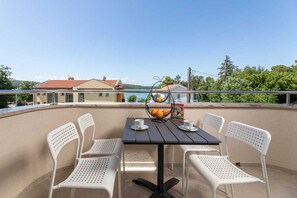 A balcony with a table and chairs, a basket of oranges, and a view of houses and trees. - Apartment Sucic Tea 5 (Soline - island Krk)