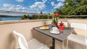 Ein Balkon mit Tisch für zwei Personen, einer Blumenvase und Blick auf den See.