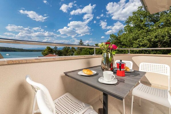 A balcony with a table set for two, a vase with flowers, and a view of the lake. - Apartment Sucic Tea 5 (Soline - island Krk)
