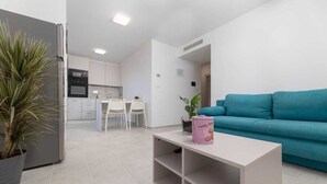 Ein modernes Wohnzimmer mit einem petrolfarbenen Sofa, einem weißen Couchtisch und einer Küchenzeile im Hintergrund.