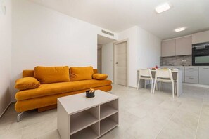 Un espace de vie compact comprenant un canapé, une petite table, un coin cuisine et une table à manger.