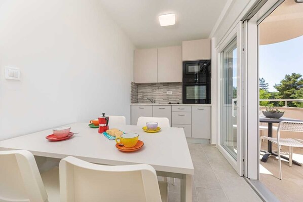Una cocina moderna con armarios blancos, un horno negro y un ventanal que da a un balcón.