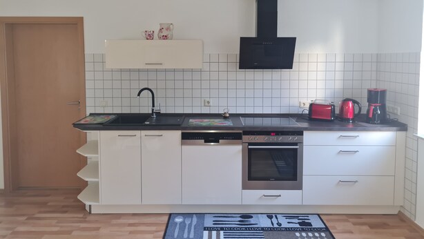 A modern kitchen with white cabinets, a black range hood, a built-in oven, a coffee maker, and a microwave. - Modernized apartment, centrally located in historic old town (Mücheln (Geiseltal))