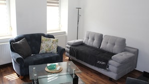 A modern living room with a dark blue sofa, a grey sofa, and a glass coffee table. - Modernized apartment, centrally located in historic old town (Mücheln (Geiseltal))