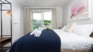 Una habitación de hotel con cama, vistas a la vegetación por la ventana y una obra de arte enmarcada en la pared.