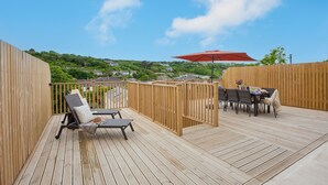 Una terraza de madera con una mesa y sillas, una sombrilla roja y vistas a un paisaje verde.