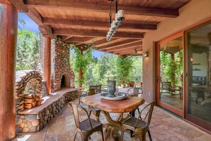 A covered patio with a stone fireplace, wooden furniture, and a glass door leading to an indoor area.