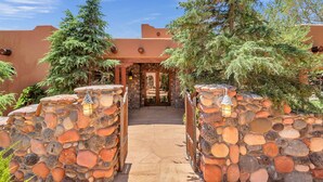 A stone-walled entrance with a wooden door, surrounded by greenery and a clear sky. - Experience luxury at Sedona Cathedral Shangri-La, a spacious 5-bedroom retreat in the Chapel Area. (Sedona)
