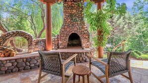 An outdoor patio with a stone fireplace, wicker chairs, and a stone wall. - Experience luxury at Sedona Cathedral Shangri-La, a spacious 5-bedroom retreat in the Chapel Area. (Sedona)