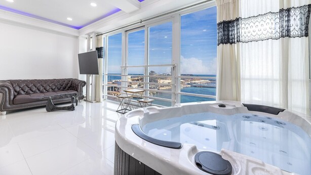 A spacious living room with a large window offering a sea view, a leather sofa, a flat-screen TV, and a hot tub. - Pohang 0.1 Poolvilla (Pohang)