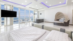 A modern hotel room with a large bed, a seating area with a view, a TV, and a balcony with a view of the sea. - Pohang 0.1 Poolvilla (Pohang)