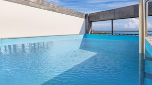 A swimming pool with a view of the sea, a concrete deck, and a large window.