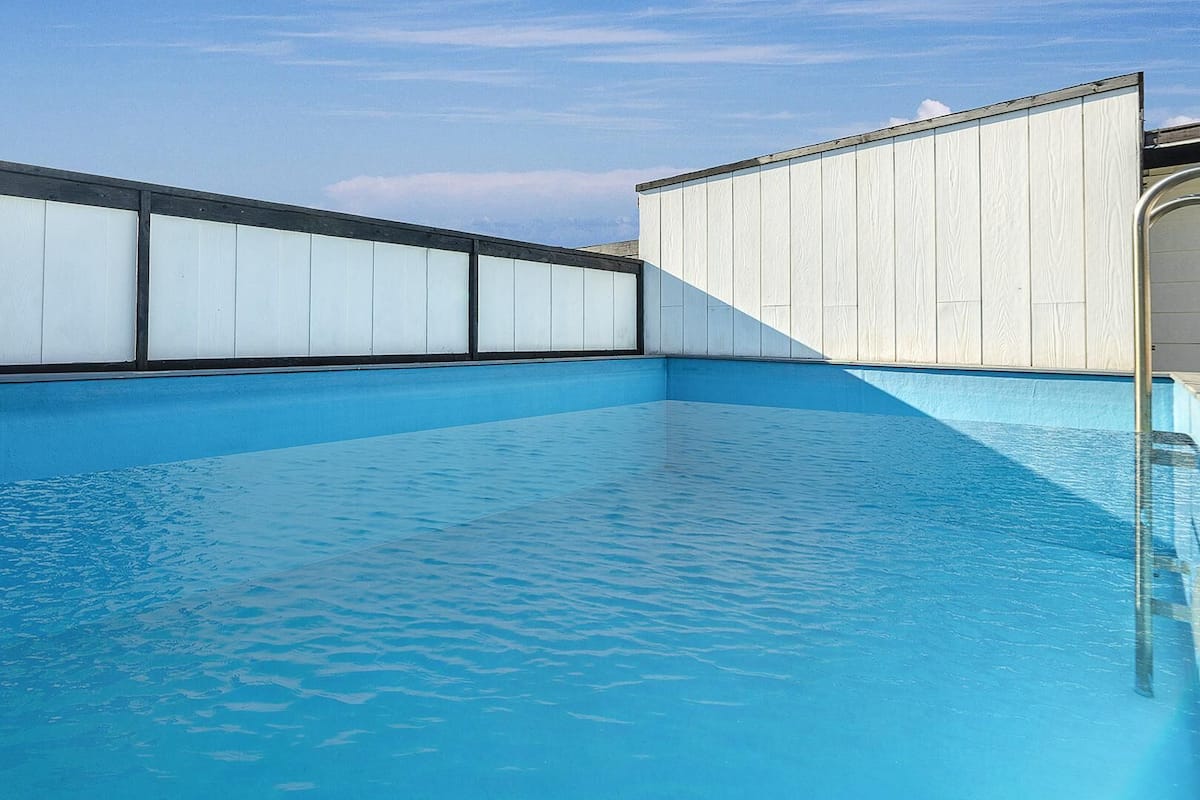 A rectangular swimming pool with clear blue water, surrounded by white walls with black trim.