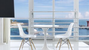 A room with a white table and two white chairs, a large window with a view of the sea and a pier. - Pohang 0.1 Poolvilla (Pohang)