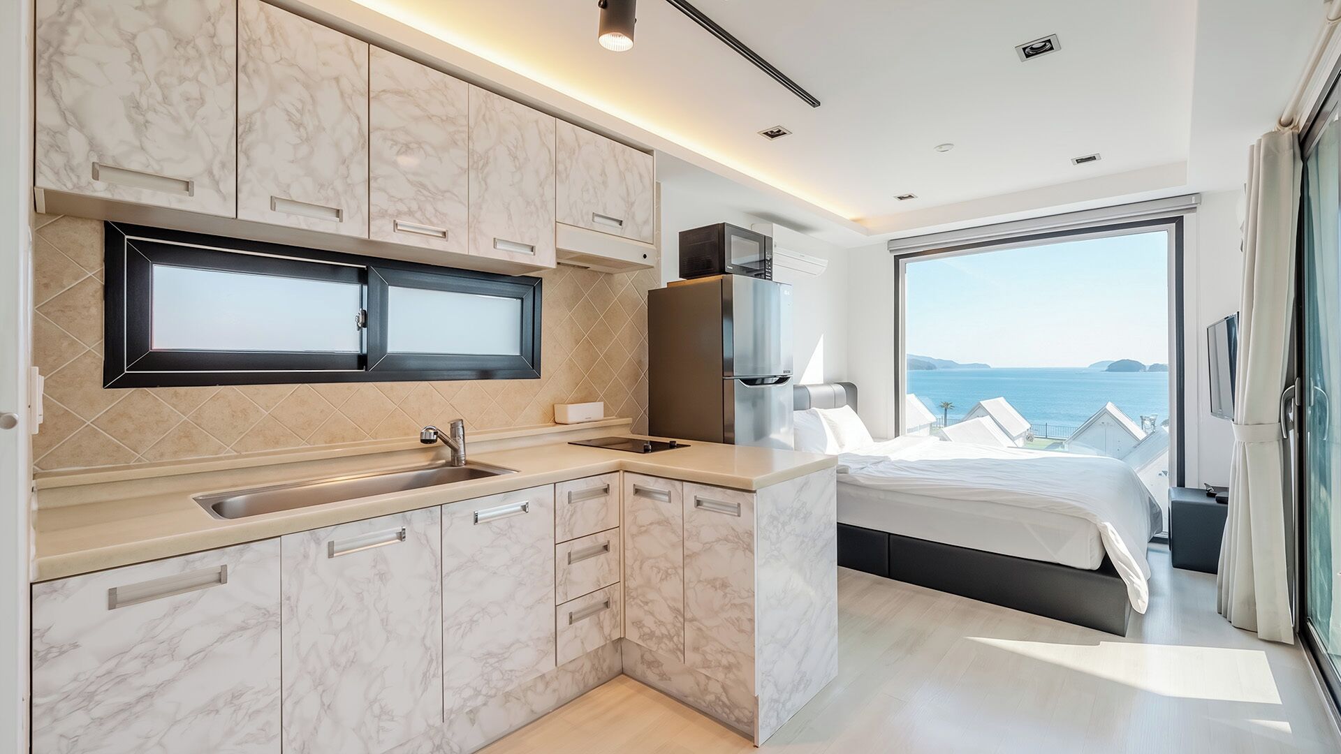 A modern kitchen with marble cabinets, a built-in microwave, and a large window overlooking the sea.