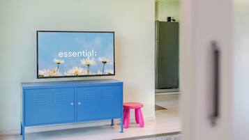 Un televisor sobre un mueble azul con un taburete rosa adelante.
