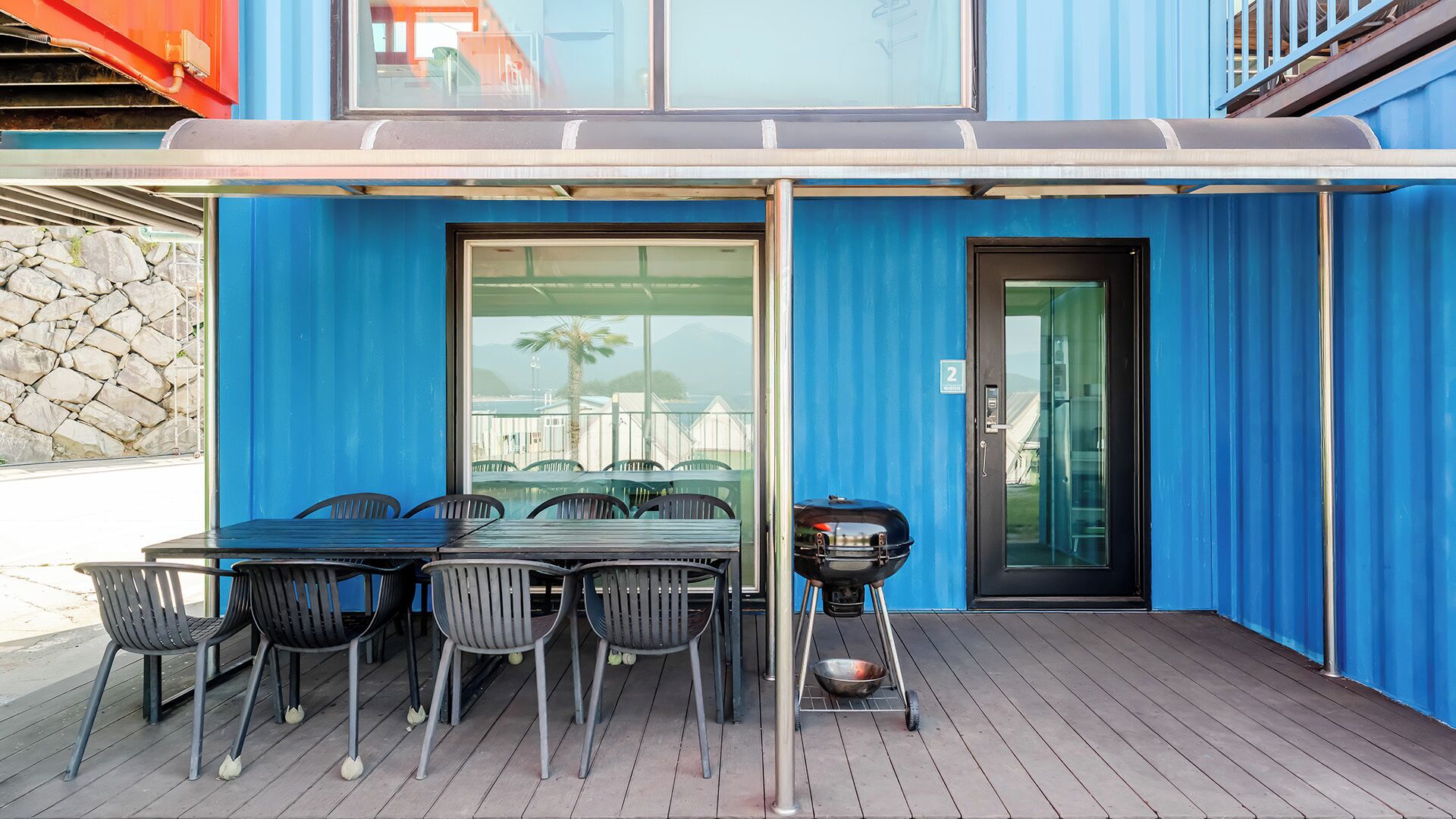 Une terrasse extérieure avec une table et des chaises, un barbecue et une porte portant un numéro.