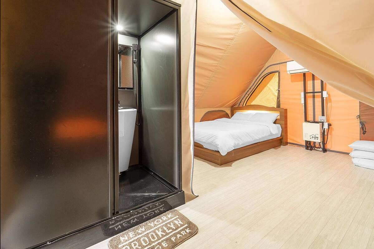 Ein Zeltraum mit Bett, kleinem Tisch und Duschbereich.