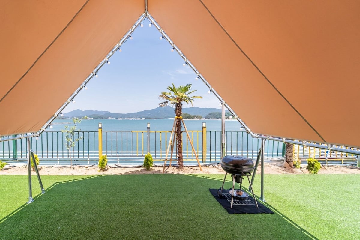 Une tente offrant une vue sur la mer et les montagnes, avec une pelouse artificielle et un barbecue.