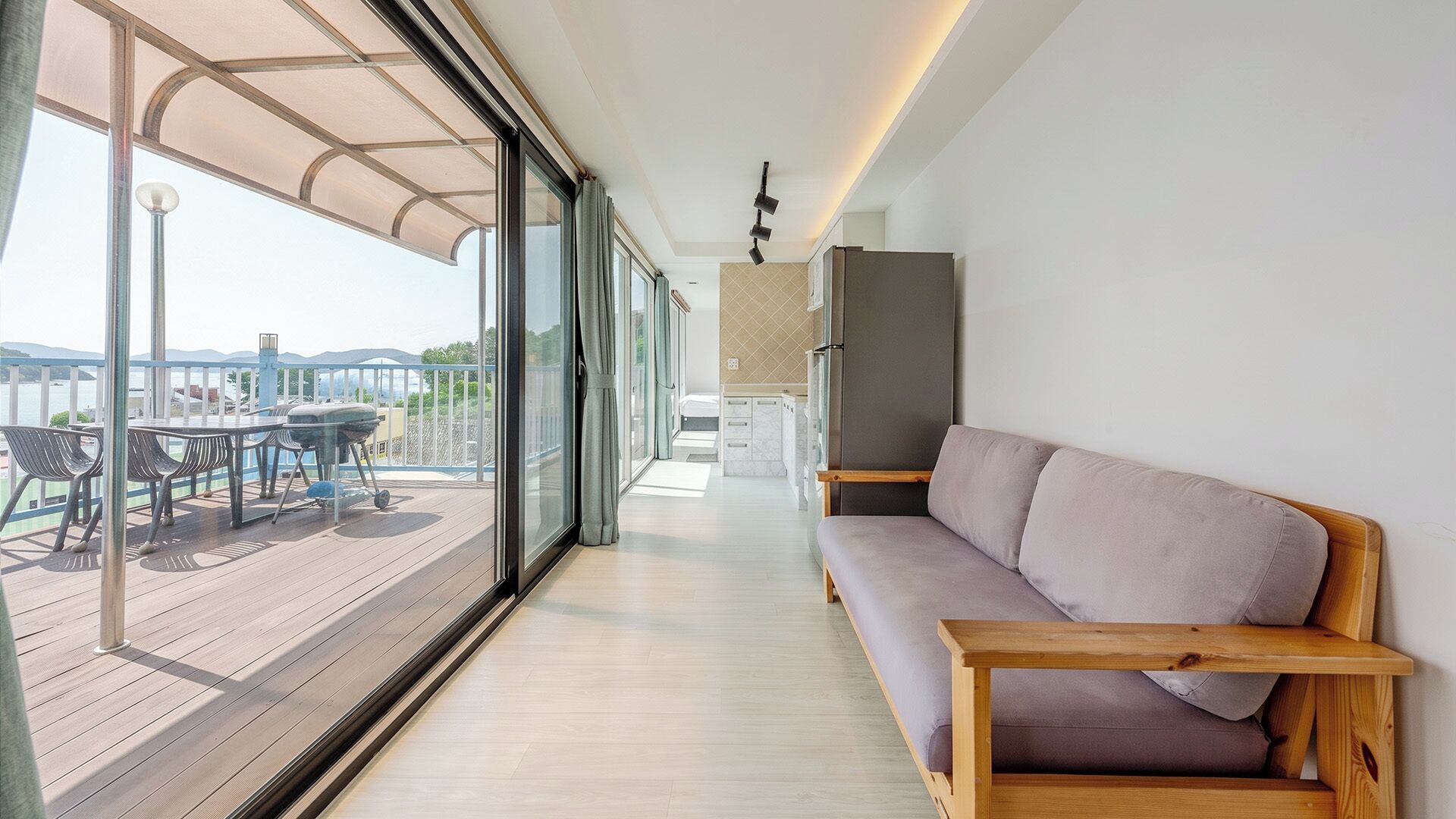 A modern interior with a wooden bench, a kitchen area, and a balcony with outdoor furniture.