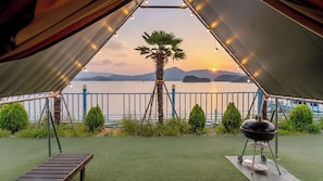 Un espacio al aire libre con carpas, vistas a un lago y montañas al atardecer.