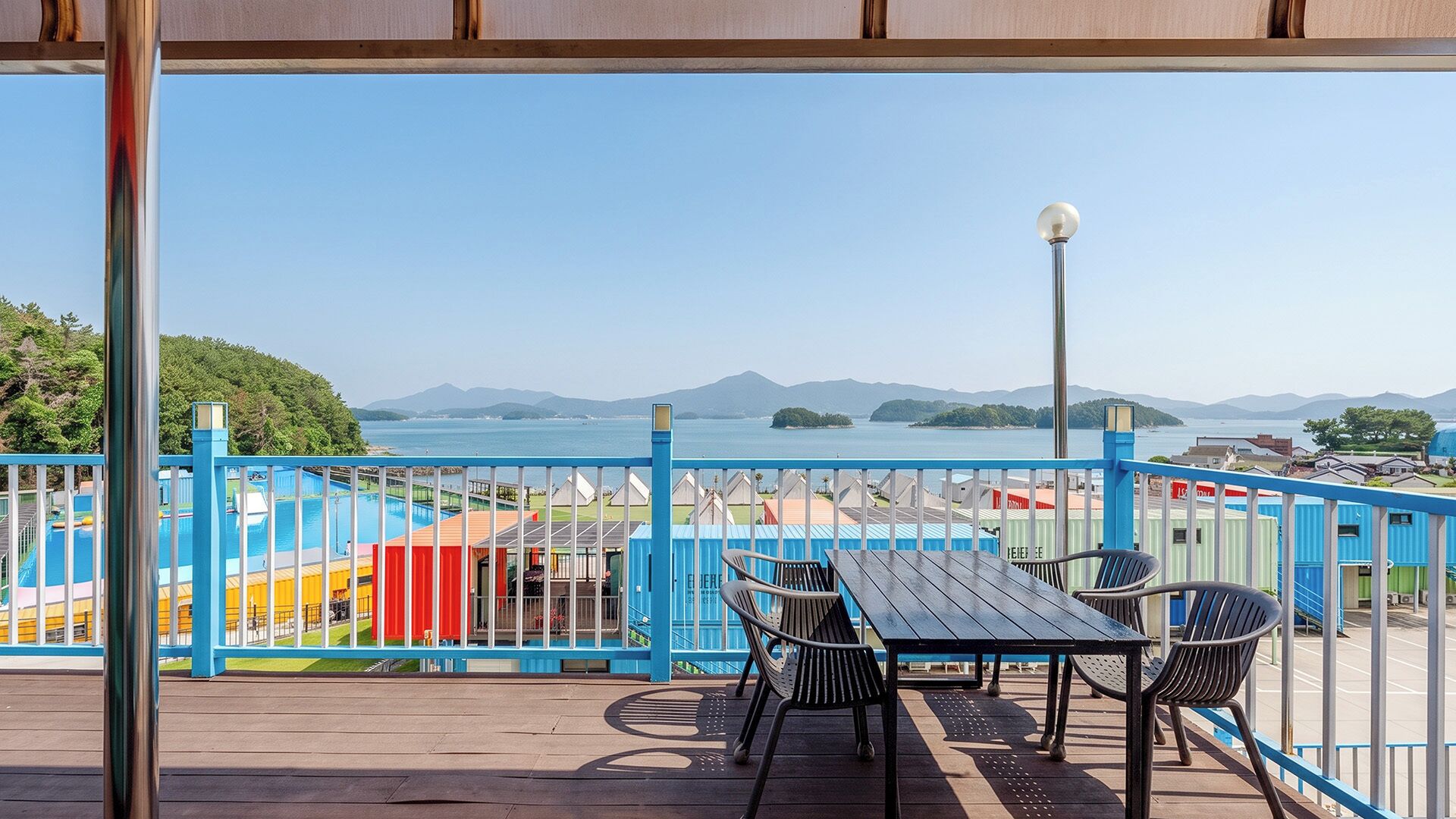 Un balcón con vistas a una piscina, sillas y un farol.