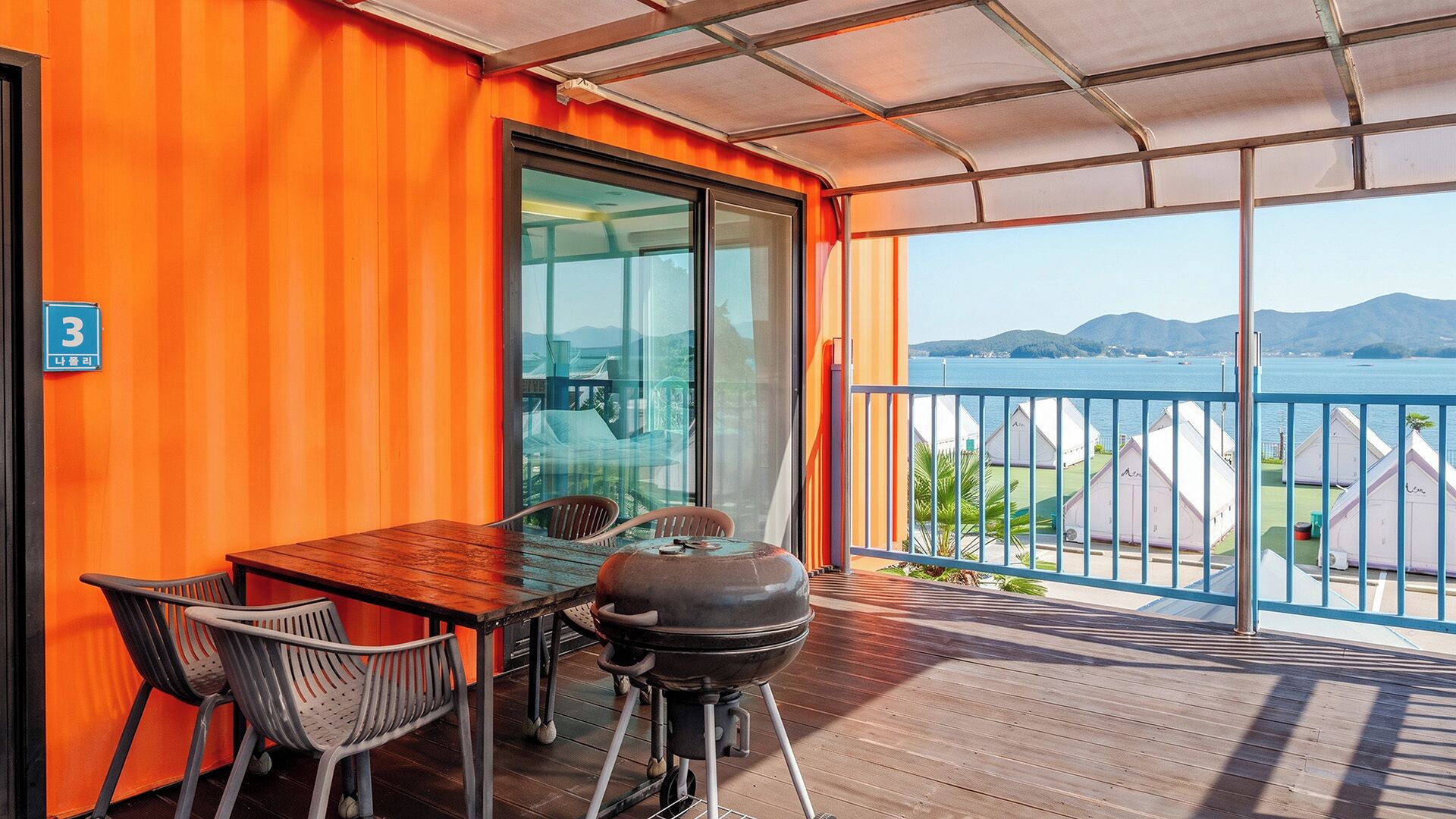 A balcony with a wooden table, chairs, and a barbecue grill.