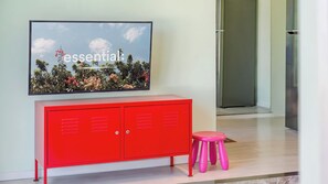 Een rode kast met twee deuren, een roze kruk en een televisie aan de muur met een natuurscène.