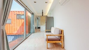 A modern hotel room with a large sliding glass door leading to an outdoor area, a wooden bench, and a small kitchenette. - Goseong Bluebeach Pension&glamping (Goseong)