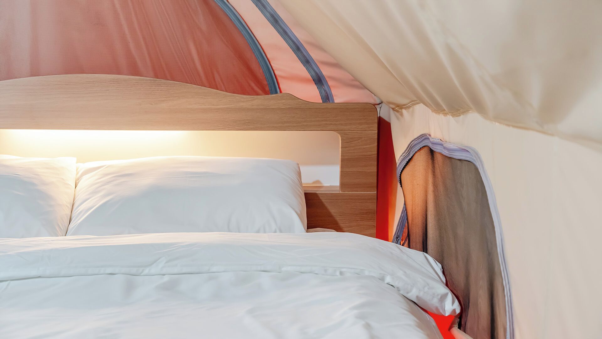 A bed with white bedding and a wooden headboard inside a tent.