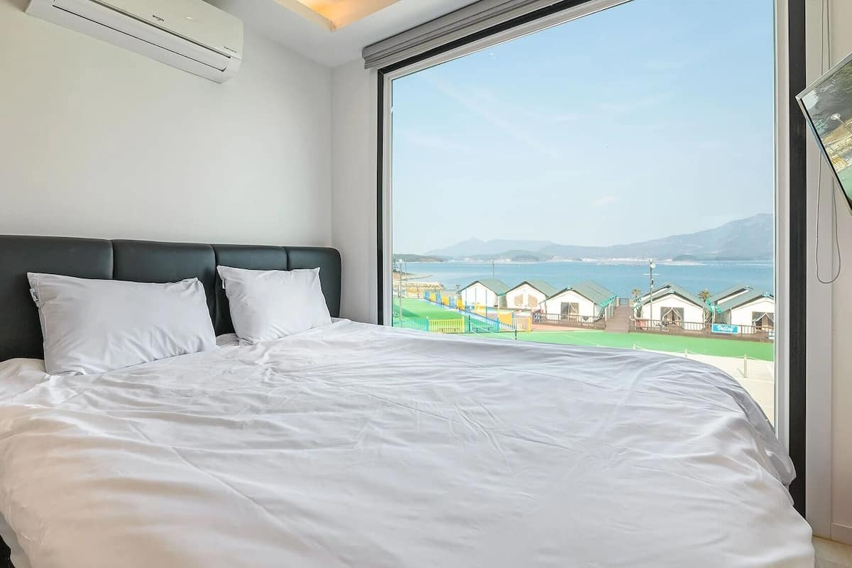 Une chambre avec un grand lit, une tête de lit noire et une vue sur une zone côtière avec des bâtiments.